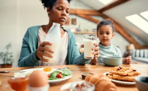 Close-up of black mother pouring a glass of milk during breakfast at home.
